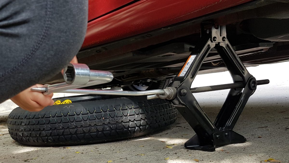 A person using a jack preparing to change a flat tire.