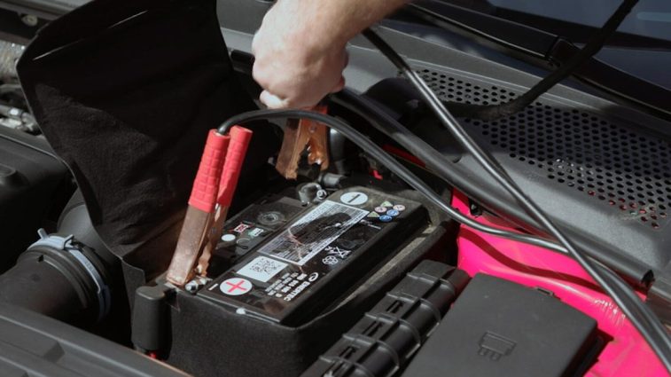 Attaching the black clamp to a car battery's negative post, with the red clamp already attached to the positive post.