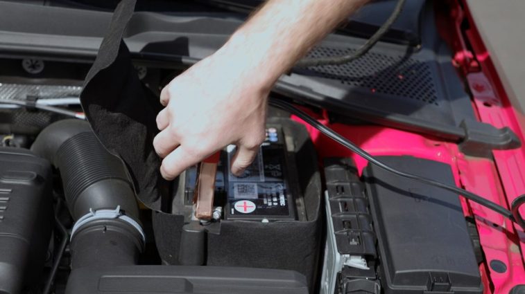 A person disconnecting the red jumper cable clamp from a car battery's positive post.