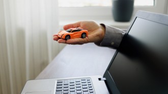 A hand holding a car by a computer.