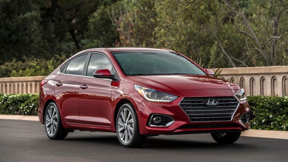 A red Hyundai Accent subcompact sedan parked in front of a decorative concrete wall. 
