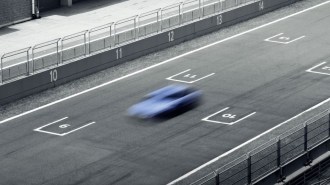 A deliberately blurred photo of a hatchback on a race track. We see the car from overhead. It appears in a shade of light blue Hyundai often uses to market its high-performance vehicles.