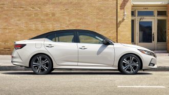 White 2023 Nissan Sentra profile near brick building.