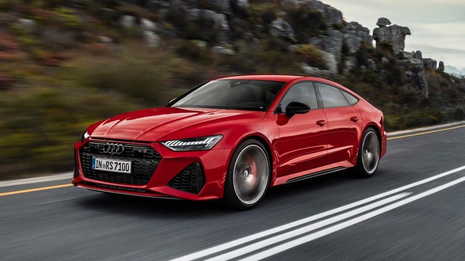 Red 2021 Audi RS7 Sportback driving on a road near rocks.