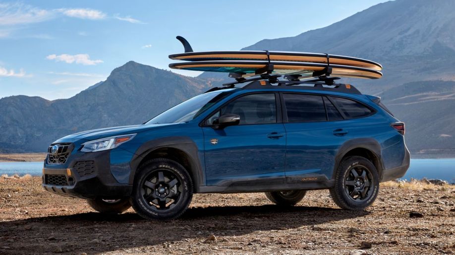 2024 Subaru Outback in blue near a lake with surfboards on the roof.
