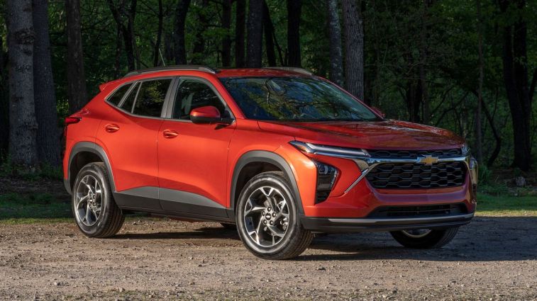 2024 Chevrolet Trax LT in Cayenne Orange Metallic parked on a gravel road in front of trees.