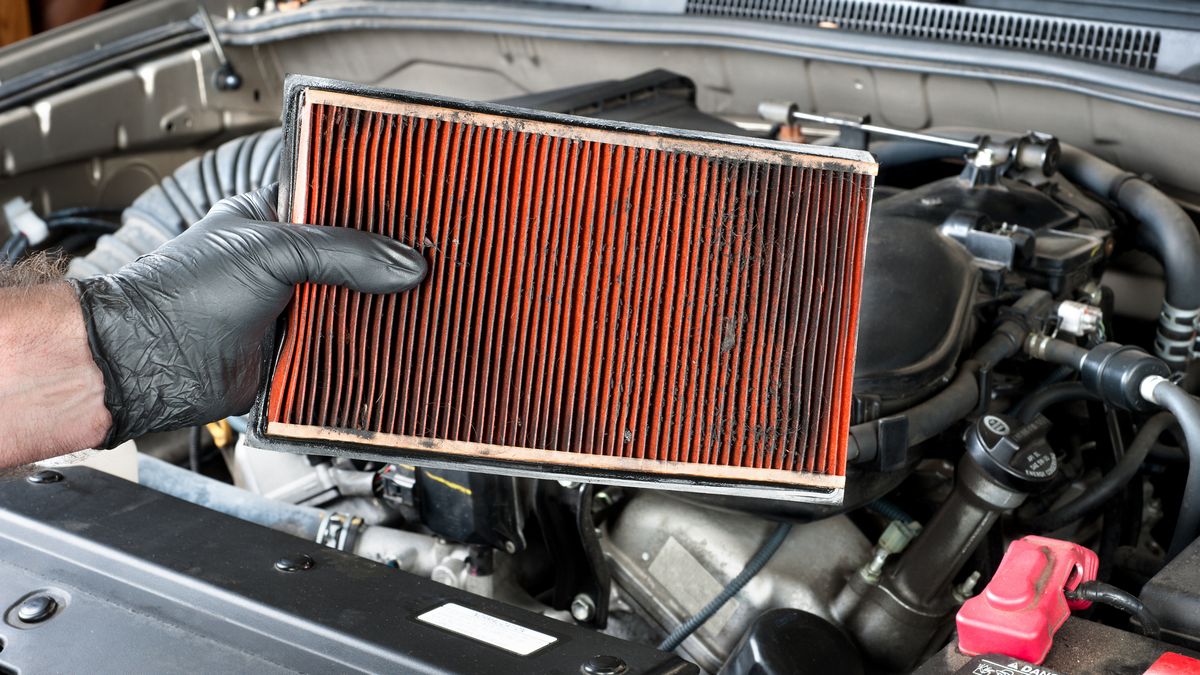 A dirty air filter held over a car engine during general auto maintenance.