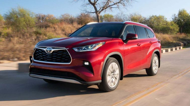 2024 Toyota Highlander Hybrid in Ruby Flare Pearl driving down a road.