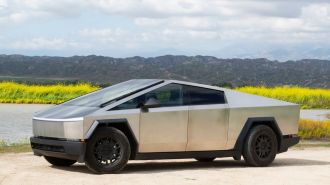 2024 Tesla Cybertruck on a dirt road with a lake and flowers in the background.