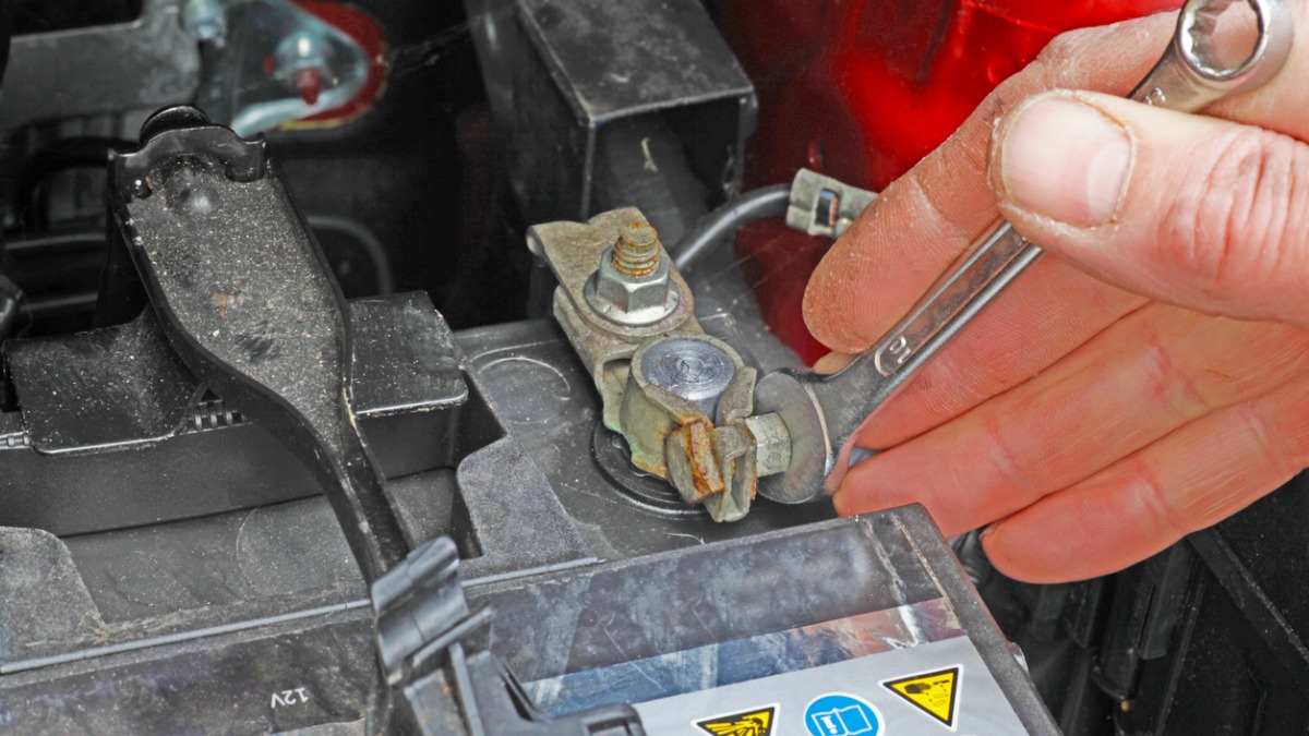 A person using a wrench to disconnect a car battery.