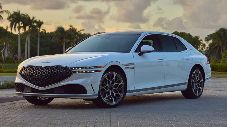 2024 Genesis G90 in white with palm trees in the background at sunset.