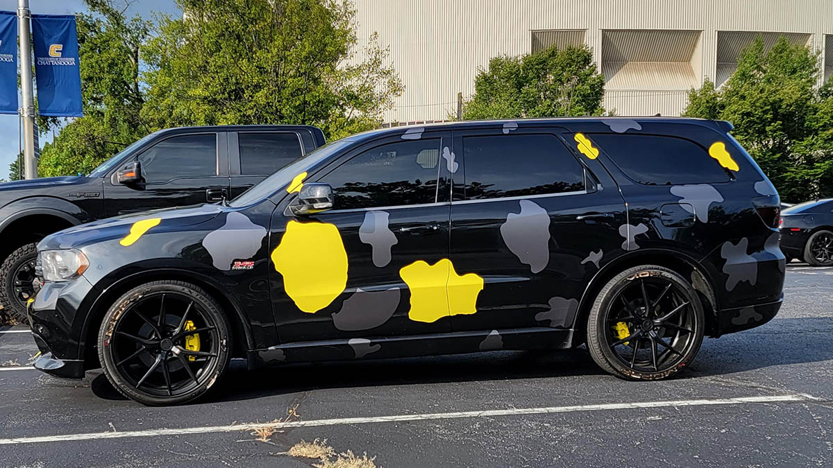 Black SUV with gray and yellow shapes on vinyl wrap.