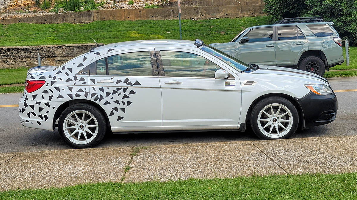 White sedan with black geometric shapes on car wrap.
