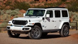 2024 Jeep Wrangler High Altitude 4xe parked on gravel near a trail.