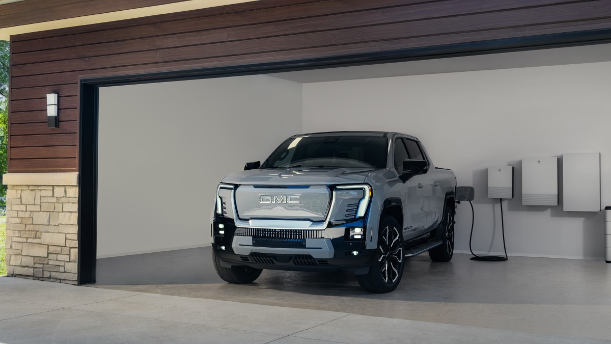 The 2025 GMC Sierra EV seen from a front quarter angle, plugged in to charge